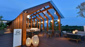 Un bar en la azotea con vigas de madera, asientos al aire libre e iluminación decorativa.