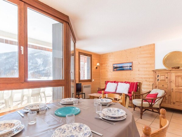 A dining area with a table set for four, wooden walls, a painting, and a view of a snowy landscape. - Spacious Apartment: 3BR, Terrace, Parking, Ski Locker, WiFi - Saint-Chaffrey (Saint-Chaffrey)