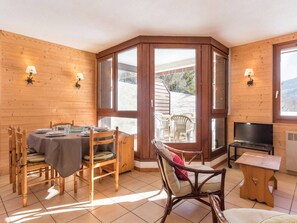 Quarto de canto com mesa de jantar posta para quatro, paredes de madeira, televisão e vista para o exterior.