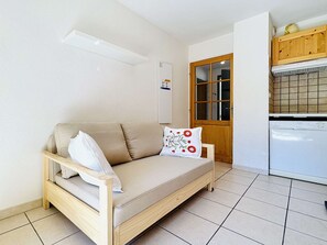 Un espacio habitable pequeño con sofá, un mueble de madera y suelo de baldosas.