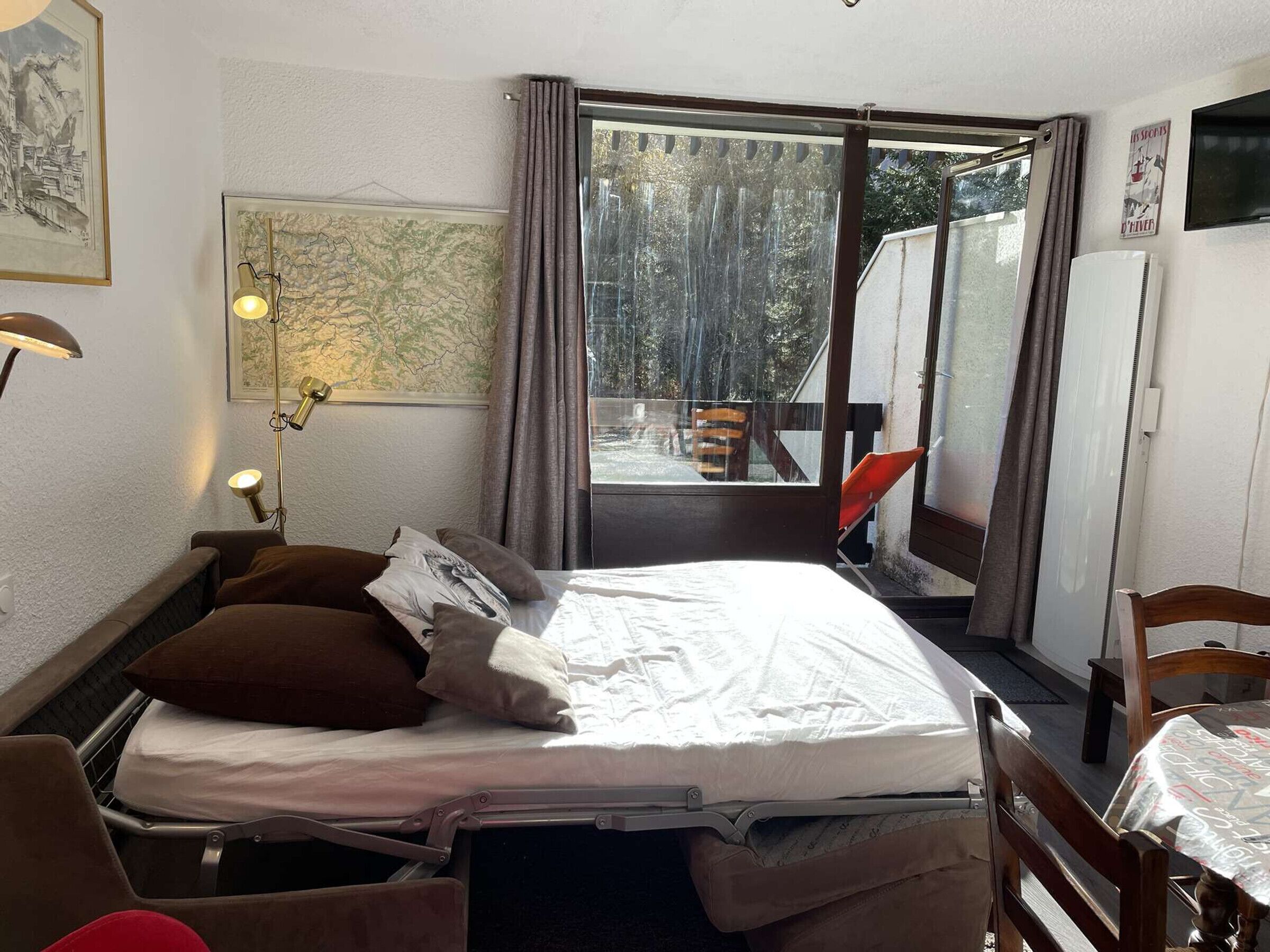 A bedroom with a bed, a desk, a chair, a map on the wall, and a window with a view of trees.