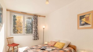 Une chambre à coucher avec une couvre-lit matelassé, une lampe de chevet, une chaise et une fenêtre avec des rideaux.