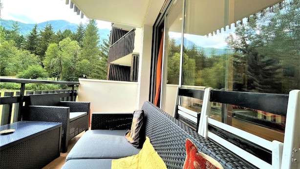 Un balcon doté de meubles en osier, d’un canapé et offrant une vue sur une région montagneuse boisée.