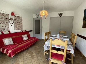 Um quarto acolhedor com um sofá vermelho, uma mesa de jantar de madeira posta para quatro pessoas e uma porta com relógio.