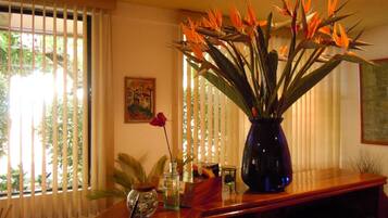 A room with a wooden table, a vase with a red rose, and a large plant with orange leaves.