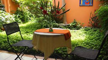 A small outdoor patio with a table covered by a tablecloth, two chairs, and a vase with flowers.