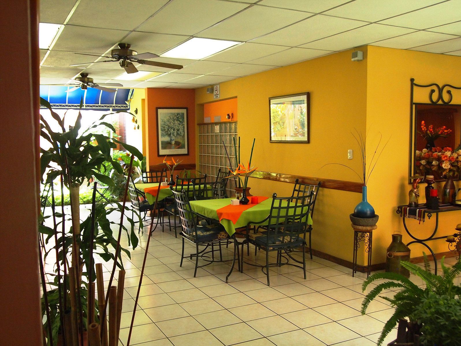 A restaurant with multiple tables, chairs, ceiling fans, and various decorations including plants and framed pictures.