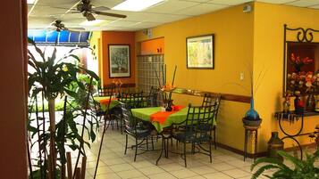 A restaurant with multiple tables, chairs, ceiling fans, and various decorations including plants and framed pictures.