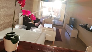 A living room with a potted orchid, a white sofa, a coffee table, and a TV on a stand. - Apartment cozy in quiet area near of beaches and shops (Manilva)