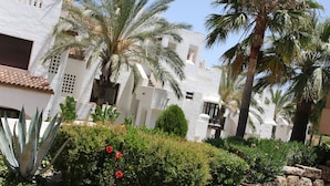 A white building with balconies, surrounded by palm trees and a garden with red flowers. - Apartment cozy in quiet area near of beaches and shops (Manilva)