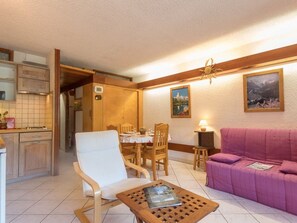 A dining area with a wooden table and chairs, a sofa, and a small table with a magazine.