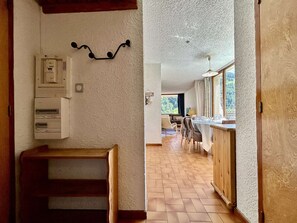 A hallway leading to a kitchen with a wooden bench, a wall-mounted electrical box, and a window with a view of greenery. - Charming 6-Pax Apt in Serre-Chevalier, South & West Balconies, Ski Locker (Saint-Chaffrey)