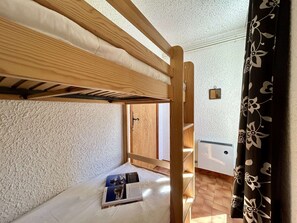 A bunk bed room with a wooden frame, a small bedside table, and a window with curtains. - Charming 6-Pax Apt in Serre-Chevalier, South & West Balconies, Ski Locker (Saint-Chaffrey)