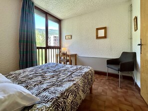 A bedroom with a bed, a chair, a desk, and a window with curtains. - Charming 6-Pax Apt in Serre-Chevalier, South & West Balconies, Ski Locker (Saint-Chaffrey)