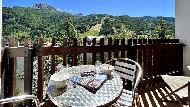 En balkon med et bord, stole og udsigt til et bjergrigt landskab.