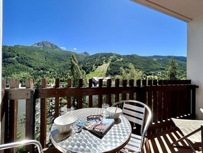 A balcony with a table, chairs, and a view of a mountainous landscape.