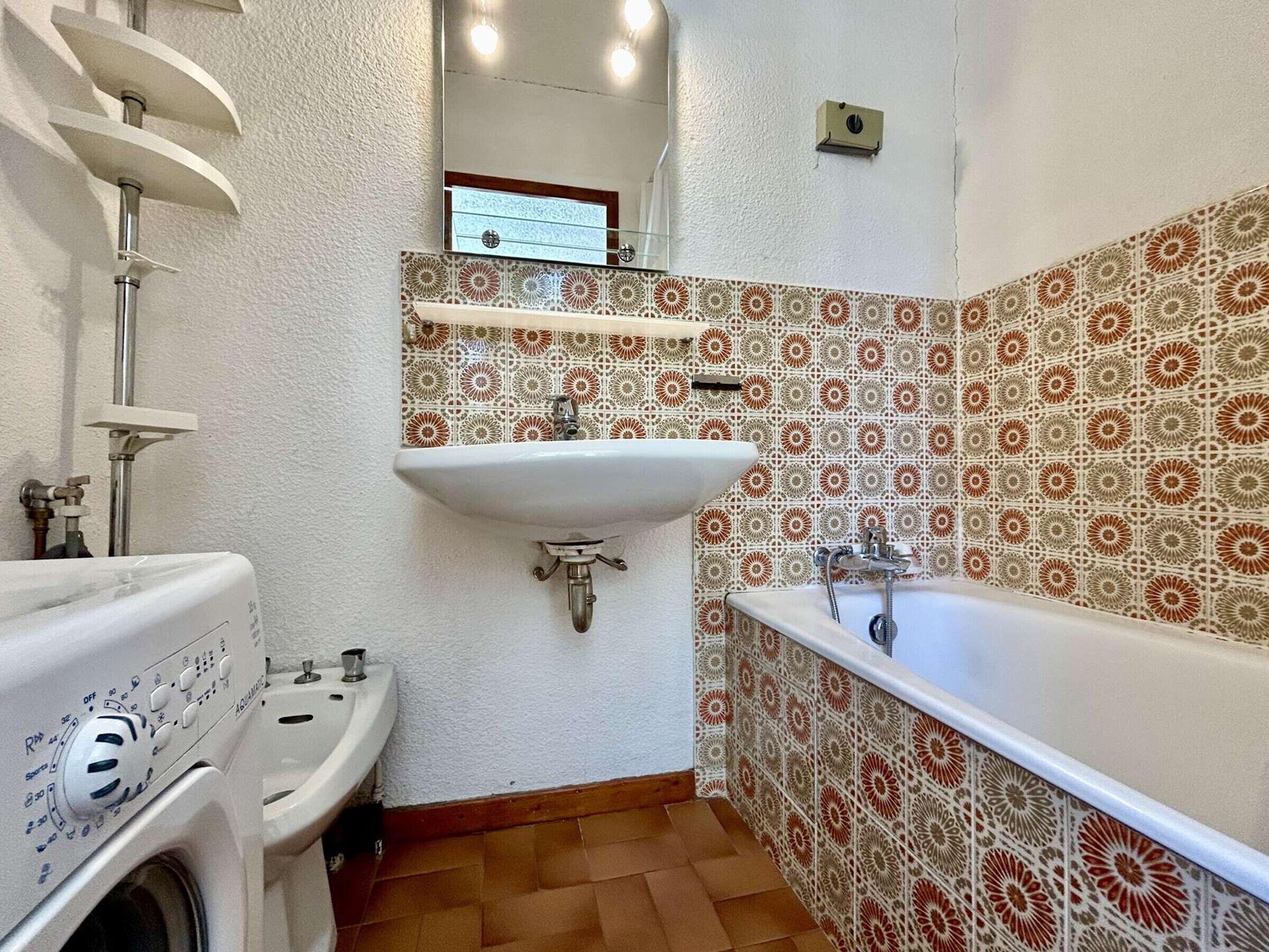 A bathroom with a washing machine, a sink, a bathtub, and patterned tiles.