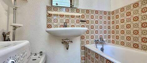 A bathroom with a washing machine, a sink, a bathtub, and patterned tiles.