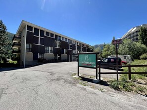 Un área de estacionamiento con un letrero que dice 'LES ÉTERLOUS PRIVATE PARKING' y un edificio con varios balcones al fondo.