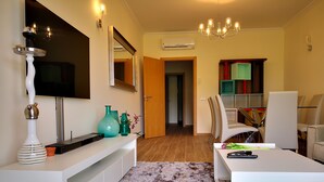 Una sala moderna con un mueble blanco para el entretenimiento, un espejo grande, una araña y vista al área de comedor.