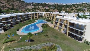 Un resort con piscina central, varios balcones y un paisaje montañoso de fondo.