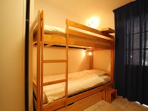 Habitación con literas de madera, un taburete pequeño y una lámpara sobre la litera superior.