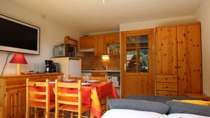 A compact room with a dining table, chairs, a sofa, a TV, and wooden cabinets. - Mountain Area Studio for 4 in Chantemerle, Serre-Chevalier (Saint-Chaffrey)