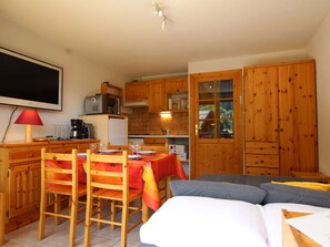 Quarto compacto com uma mesa de jantar, cadeiras, um sofá, uma TV e armários de madeira.