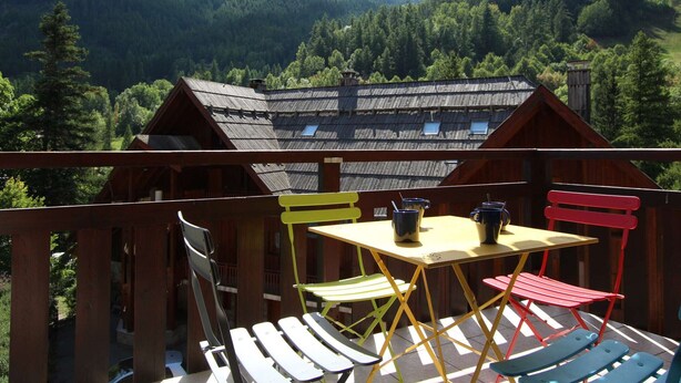 A wooden cabin with a balcony, a table, and colorful chairs. - Mountain Area Studio for 4 in Chantemerle, Serre-Chevalier (Saint-Chaffrey)