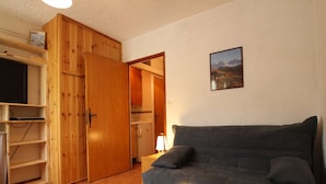 Een gezellige woonkamer met een grijze bank, een houten kast en een keuken op de achtergrond.