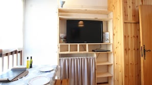 Een kleine kamer met een houten tv-meubel, een tafel met borden en bestek, en een gordijn.