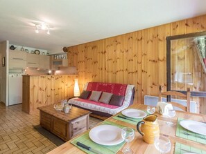 Una habitación acogedora con pared de madera, un sofá, una mesa de comedor para dos personas y una zona de cocina al fondo.