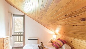 A bedroom with two beds, a wooden ceiling, a nightstand with a lamp, and a view of the outdoors through a door. - Charming 3-room apt for 6 with parking, near slopes and center (Le Monêtier-les-Bains)