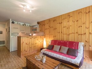 Una habitación acogedora con pared de madera, kitchenette, sofá con cojines y una mesa de centro con jarras y vasos.