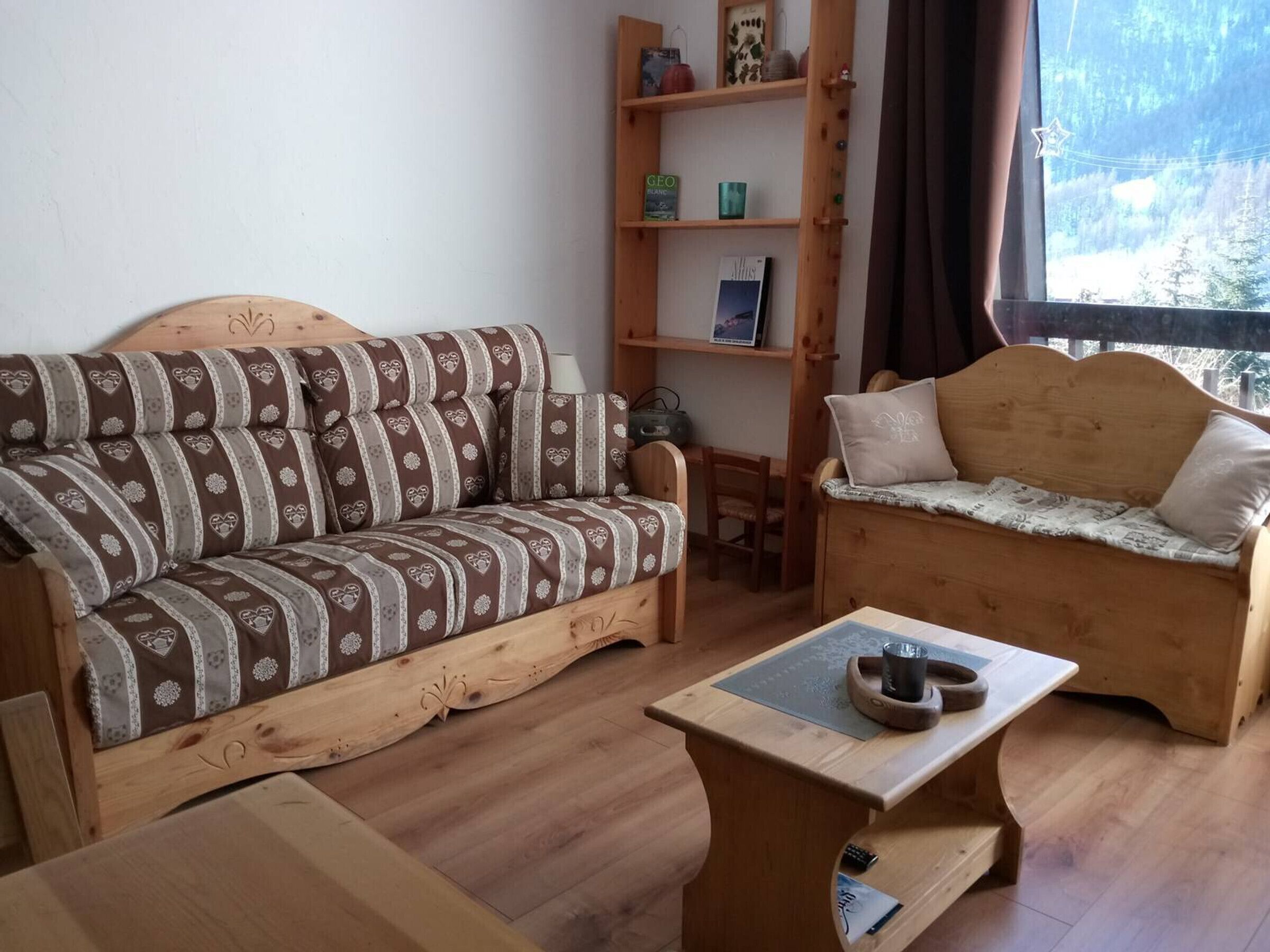 A cozy living room with a brown sofa and a wooden bench, a small table with a cup, and a bookshelf against the wall.