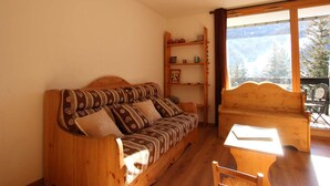 A cozy room with a wooden sofa, a wooden chair, a small table, and a shelf with various items.