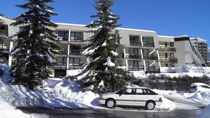 A multi-story hotel with balconies, surrounded by snow-covered trees and parked cars.