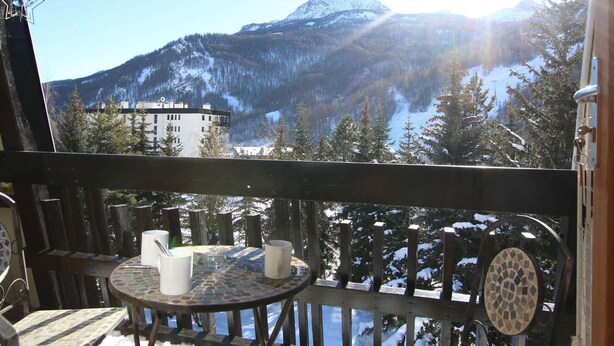 A balcony with a view of a mountain, a building, and snow-covered trees.