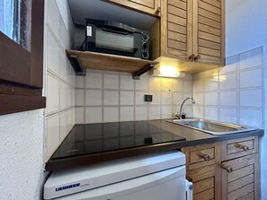 A compact kitchen with a built-in microwave, a sink, and wooden cabinetry. - Cozy Studio Near Briançon Center and Ski Lift (Briançon)