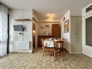 A room with a dining table, chairs, a TV mounted on the wall, a wooden cabinet, and a door.