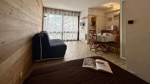 Ett rum med en väggpanel av trä, en soffa, ett matbord med stolar och en köksdel.