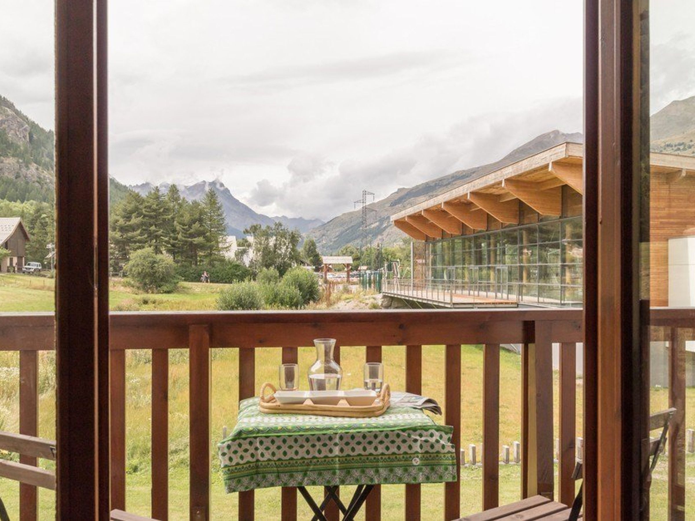 A balcony with a table set for tea, overlooking a mountainous landscape and a modern building.