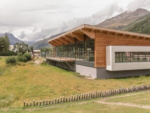 Un edifici modern amb façana de fusta i grans finestres, amb les muntanyes al fons.