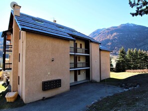 Un edificio de dos pisos con techo inclinado, un pequeño espacio para sentarse al aire libre y un buzón.