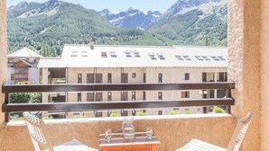 A balcony with a view of a mountain range and a building with multiple windows. - Cozy 2-Room Apartment with Mountain Views, Balcony & Close to Ski Lifts in Le Monêtier-les-Bains (Le Monêtier-les-Bains)