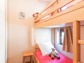 Una cama litera con ventana, un taburete de madera pequeño y un peluche en la cama.