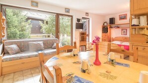 A cozy room with a sofa, a dining table with a vase, and a TV. - Charming Studio with Garden, Sleeps 4, South-Facing in Serre-Chevalier (Saint-Chaffrey)