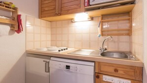 A compact kitchen with wooden cabinets, a microwave, a dishwasher, and a sink. - Charming Studio with Garden, Sleeps 4, South-Facing in Serre-Chevalier (Saint-Chaffrey)