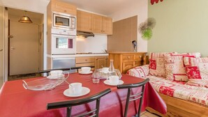 A compact kitchen with modern appliances, a dining table with chairs, and a cozy seating area with patterned cushions. - Cozy 2-Room Apartment for 4-6, Near Prorel Cable Car, South-Facing Balcony, Ski Locker (Briançon)