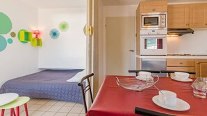A compact kitchen with a microwave, oven, and a small refrigerator. There is a dining table with a red tablecloth and a few chairs. - Cozy 2-Room Apartment for 4-6, Near Prorel Cable Car, South-Facing Balcony, Ski Locker (Briançon)
